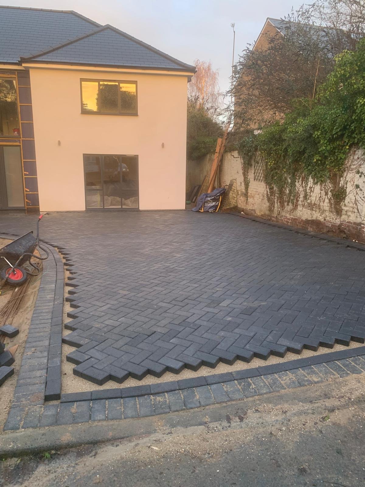 Charcoal block paving driveway with contrasting edging beside a cream house