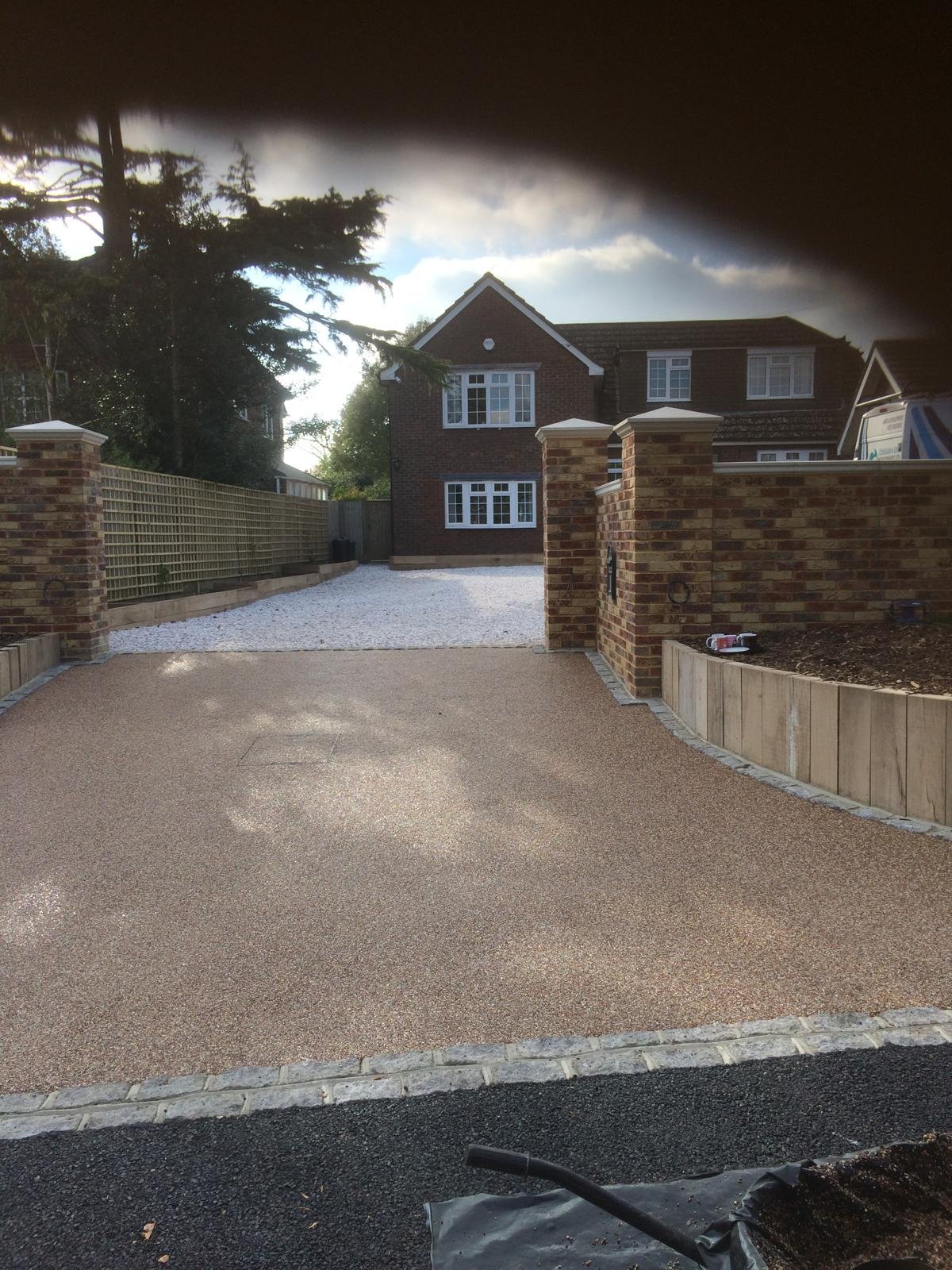 Resin bound driveway leading between stone walls to a brick home